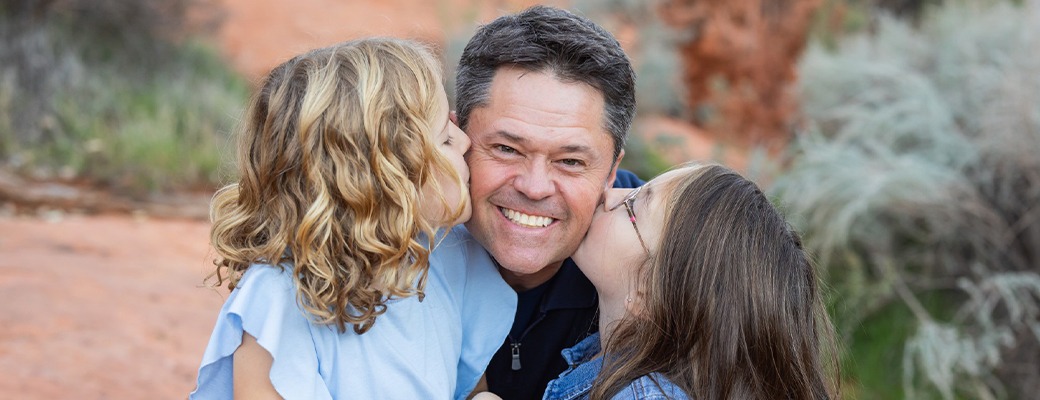 Image of Justin Osmond with his two young daughters kissing him on the cheek